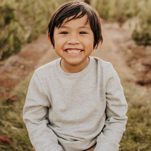 A boy smiling at the Christmas tree farm during Christmas mini photo sessions in San Antonio.