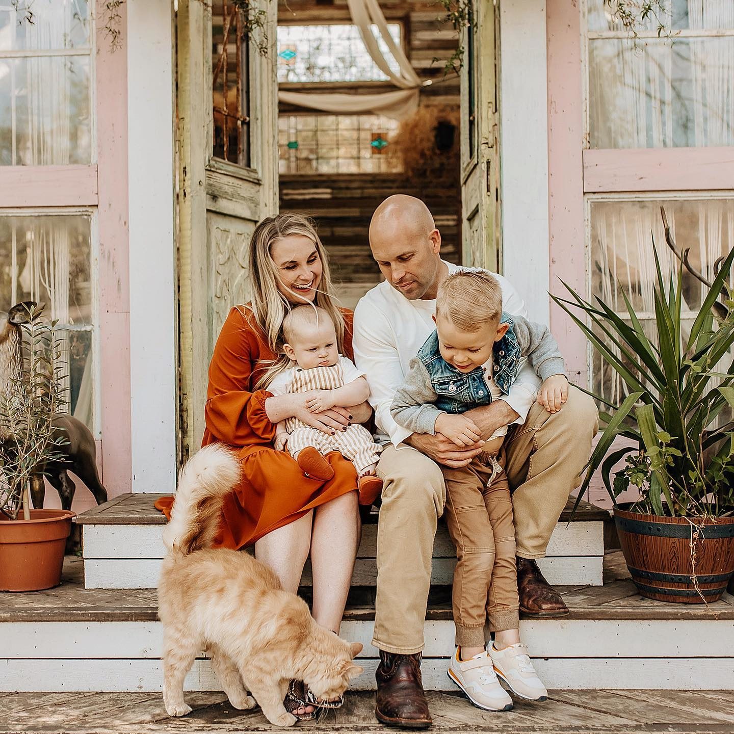 A family of 4 and their orange cat at a pink greenhouse for spring family mini sessions.