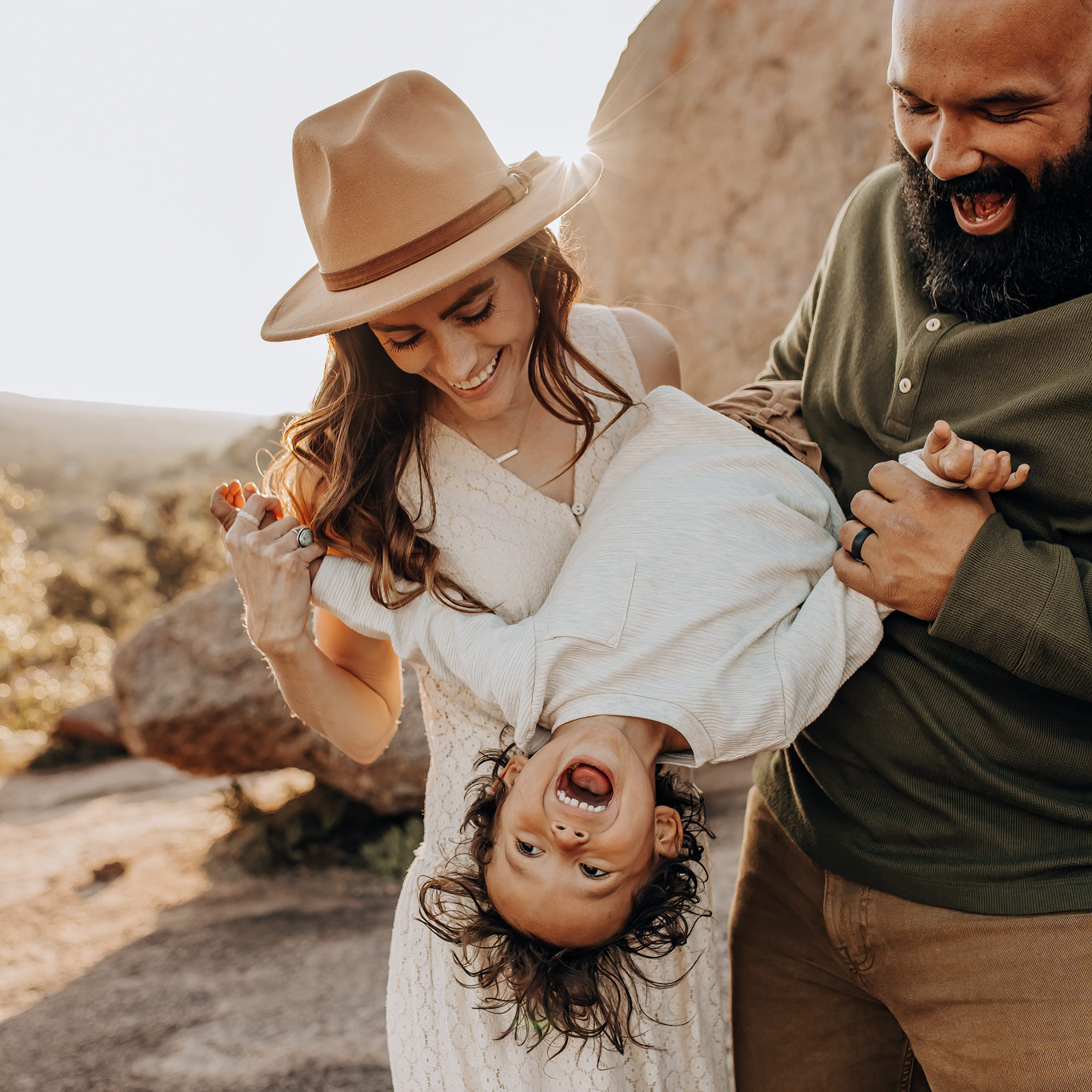Family photography session at Enchanted Rock State Natural Area with a mom and dad holding a son upside down playfully, while the boy is laughing.