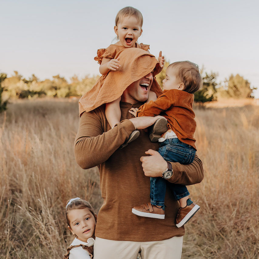 A father holding his three children in a field of tall grasses and golden tones for a family photoshoot.